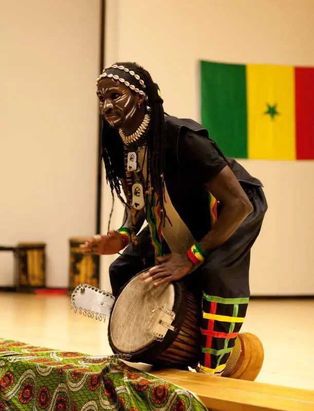 Kasvonsa maalannut rumpali soittaa djembeä Senegalin lipun edessä