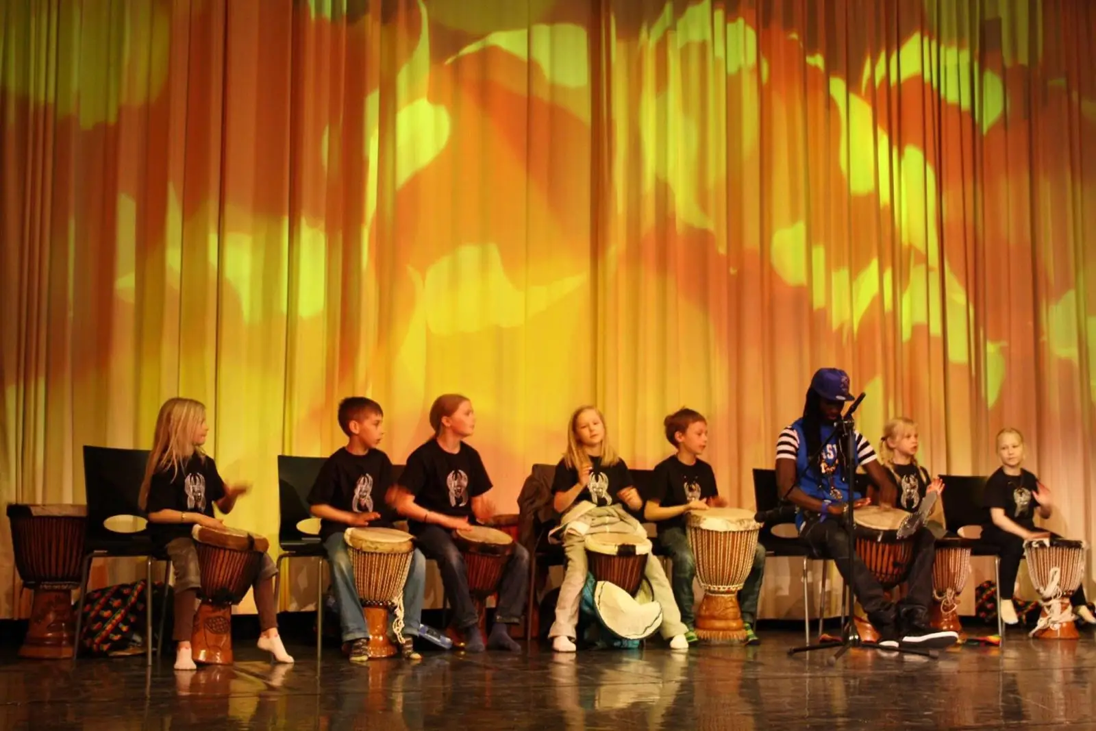 Koululaiset opettelevat soittamaan djembe-rumpuja lavalla